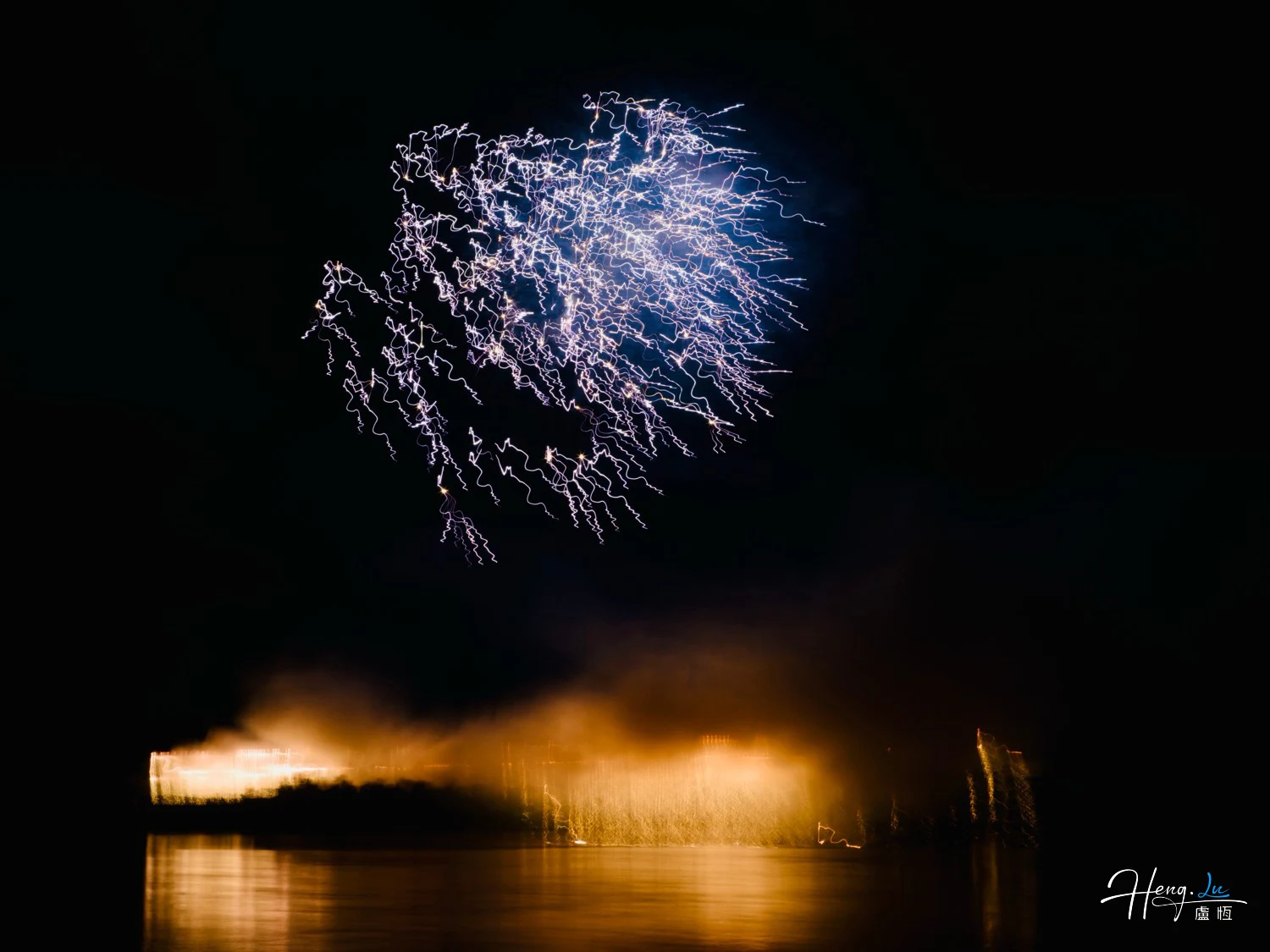 Blue-fireworks-illuminating-night-sky-over-water