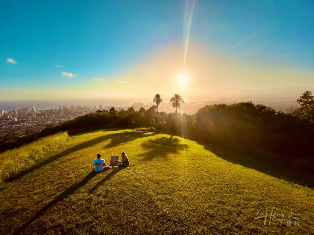 Couple-sitting-on-green-hill-overlooking-city-sunset